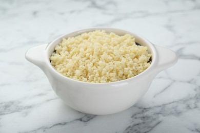 Photo of Bowl of tasty couscous on white marble table, closeup