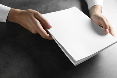 Photo of Man holding blank notebook at black textured table, closeup. Mockup for design