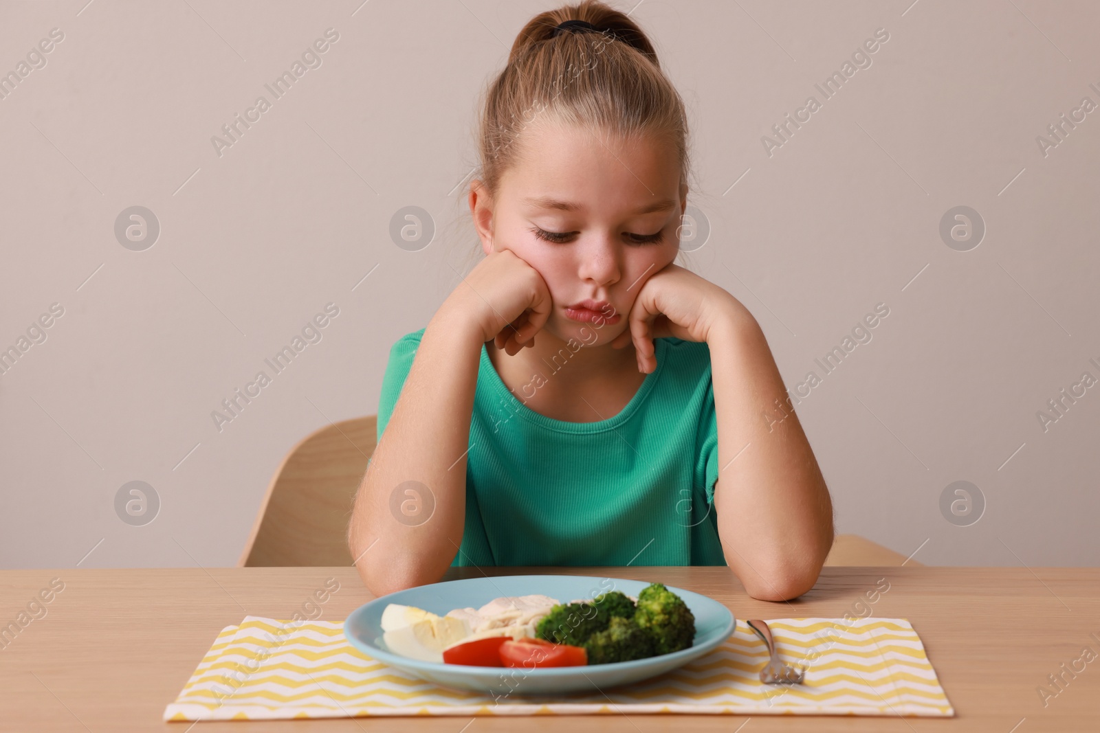 Photo of Cute little girl refusing to eat her breakfast at table on grey background