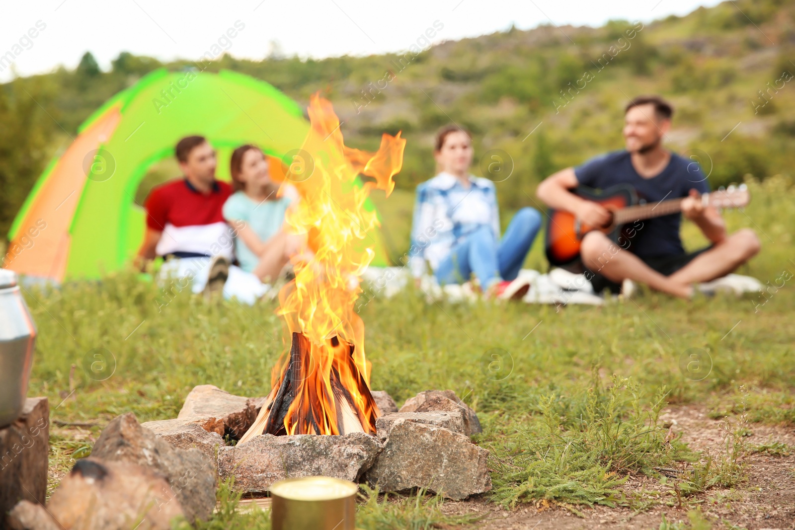 Photo of Group of people resting outdoors, focus on bonfire. Camping season