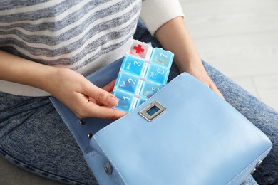 Photo of Woman putting pill box into bag indoors, closeup