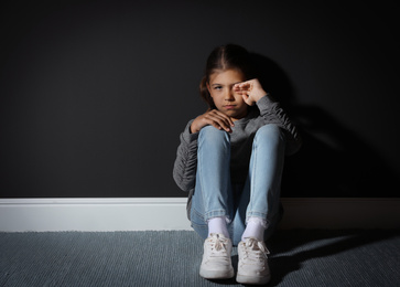 Sad little girl near black wall. Domestic violence concept