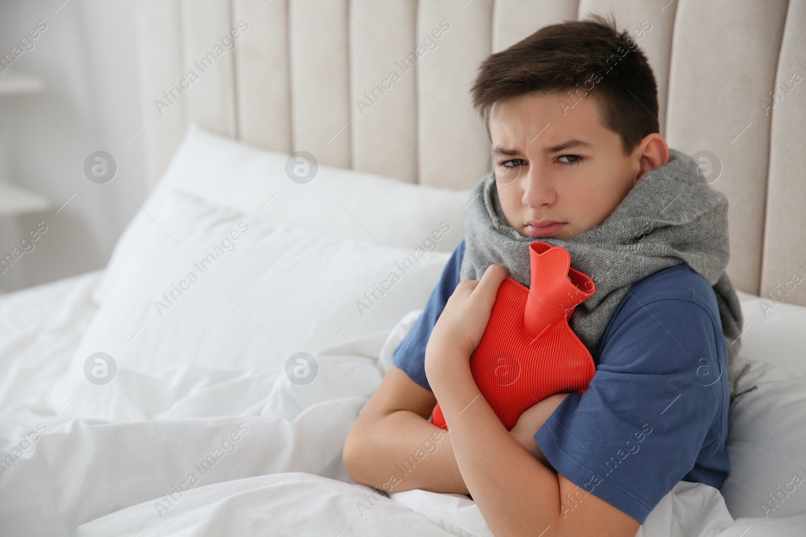 Photo of Sick teenage boy with hot water bottle in bed at home. Space for text