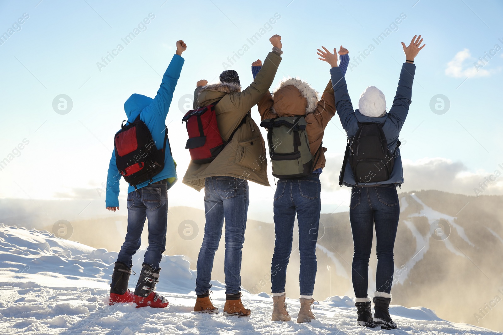 Photo of Group of excited friends with backpacks enjoying mountain view during winter vacation