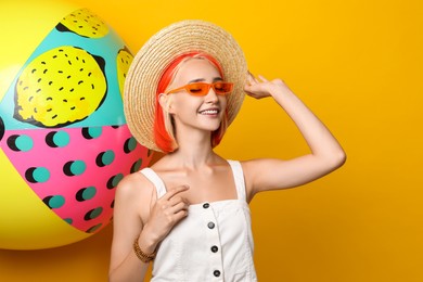 Photo of Beautiful young woman with bright dyed hair and inflatable ball on orange background