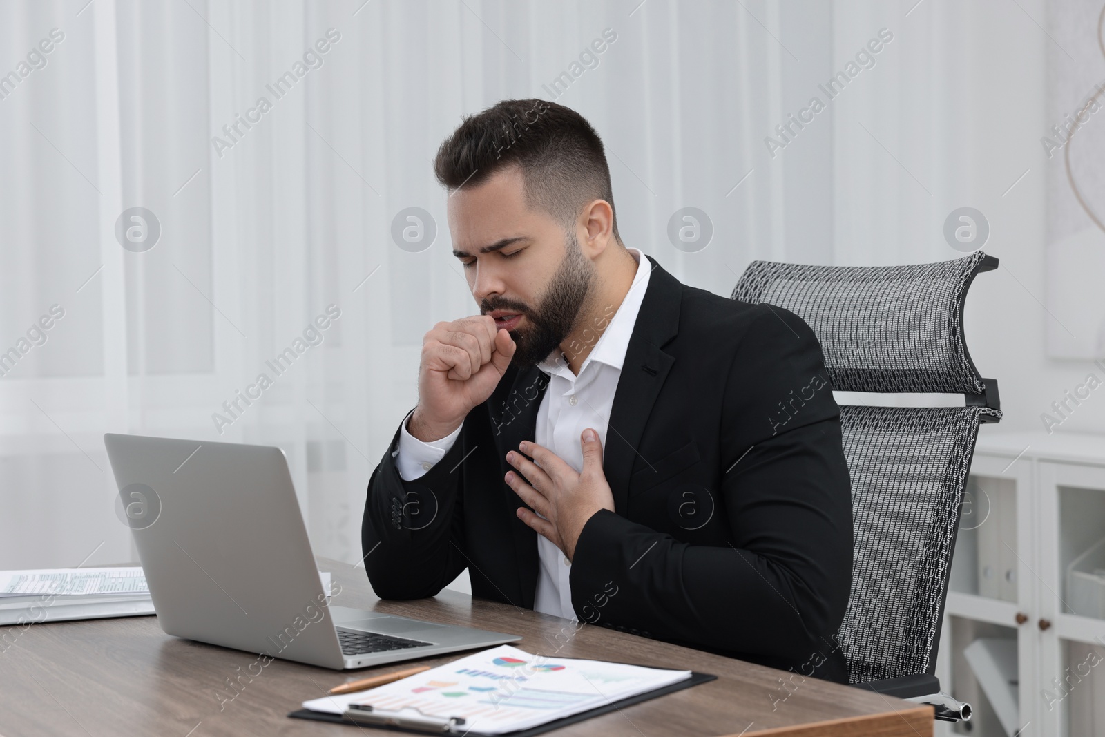 Photo of Sick man coughing at workplace in office