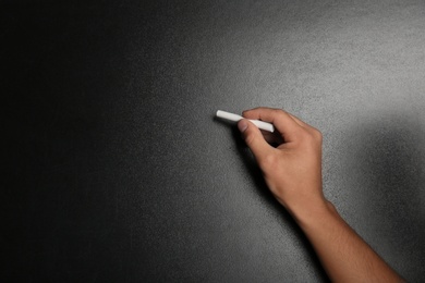 Photo of Man writing with piece of chalk on blackboard