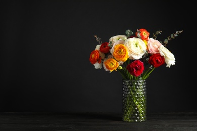 Photo of Vase with beautiful spring ranunculus flowers on table against dark background. Space for text