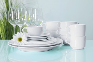 Set of clean dishware and flower on light blue table, closeup