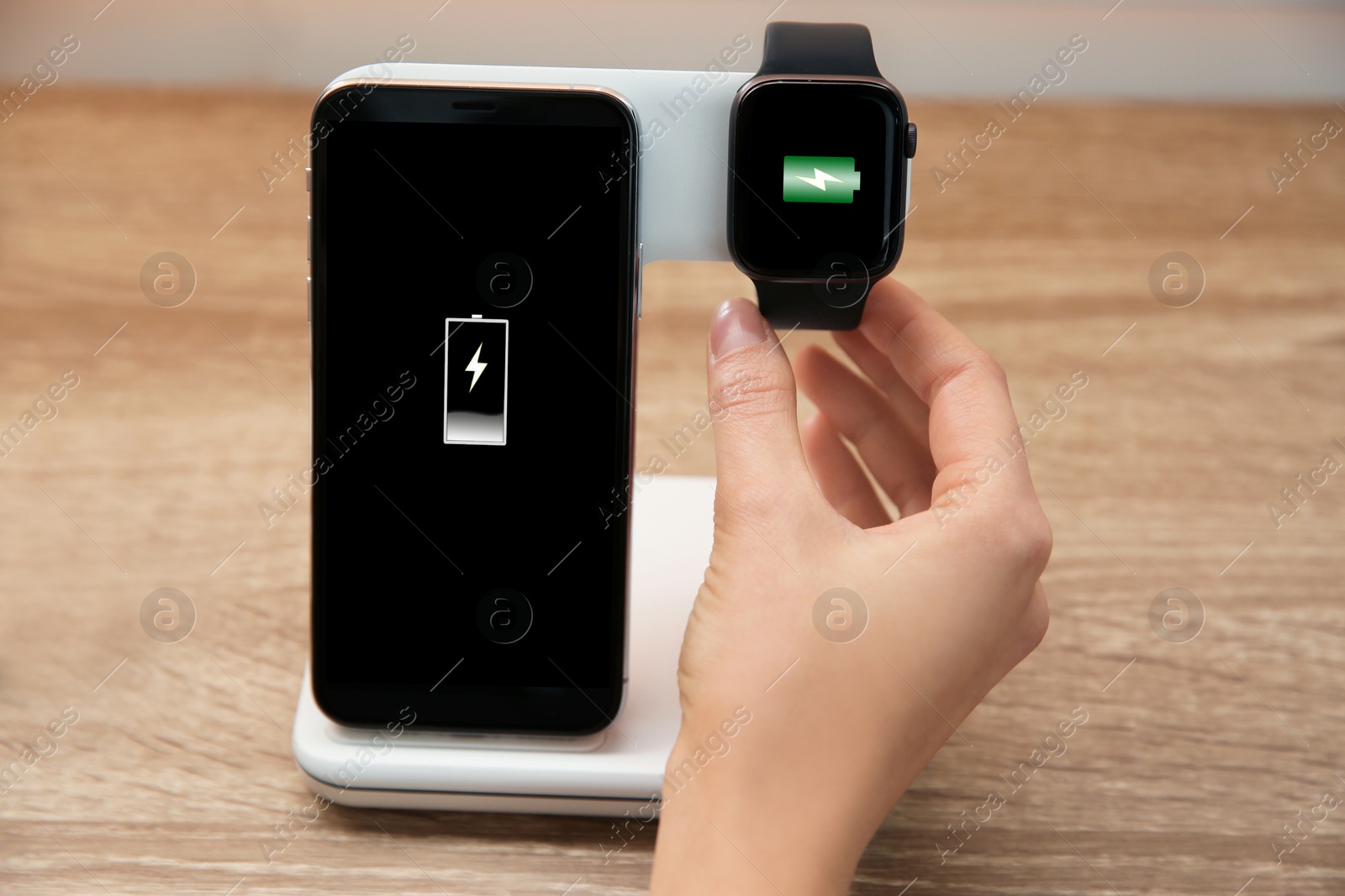 Photo of Woman putting smartwatch onto wireless charger at wooden table, closeup. Modern workplace accessory