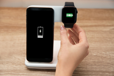 Woman putting smartwatch onto wireless charger at wooden table, closeup. Modern workplace accessory