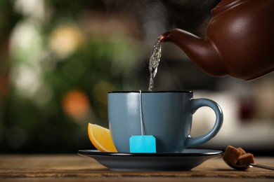 Photo of Pouring hot water into cup with tea bag at wooden table against blurred background