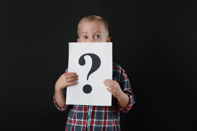 Boy holding sheet of paper with question mark on black background