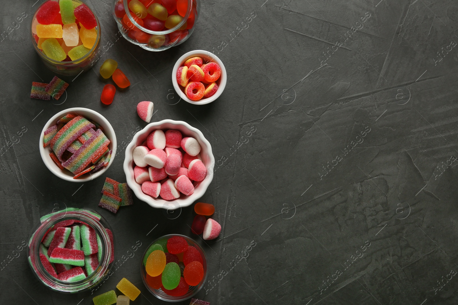 Photo of Flat lay composition with bowls of different jelly candies on black stone background. Space for text