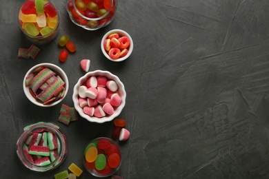 Photo of Flat lay composition with bowls of different jelly candies on black stone background. Space for text