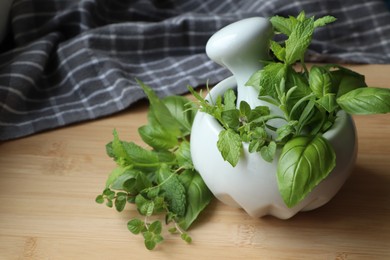 Mortar with different fresh herbs on wooden table, closeup. Space for text
