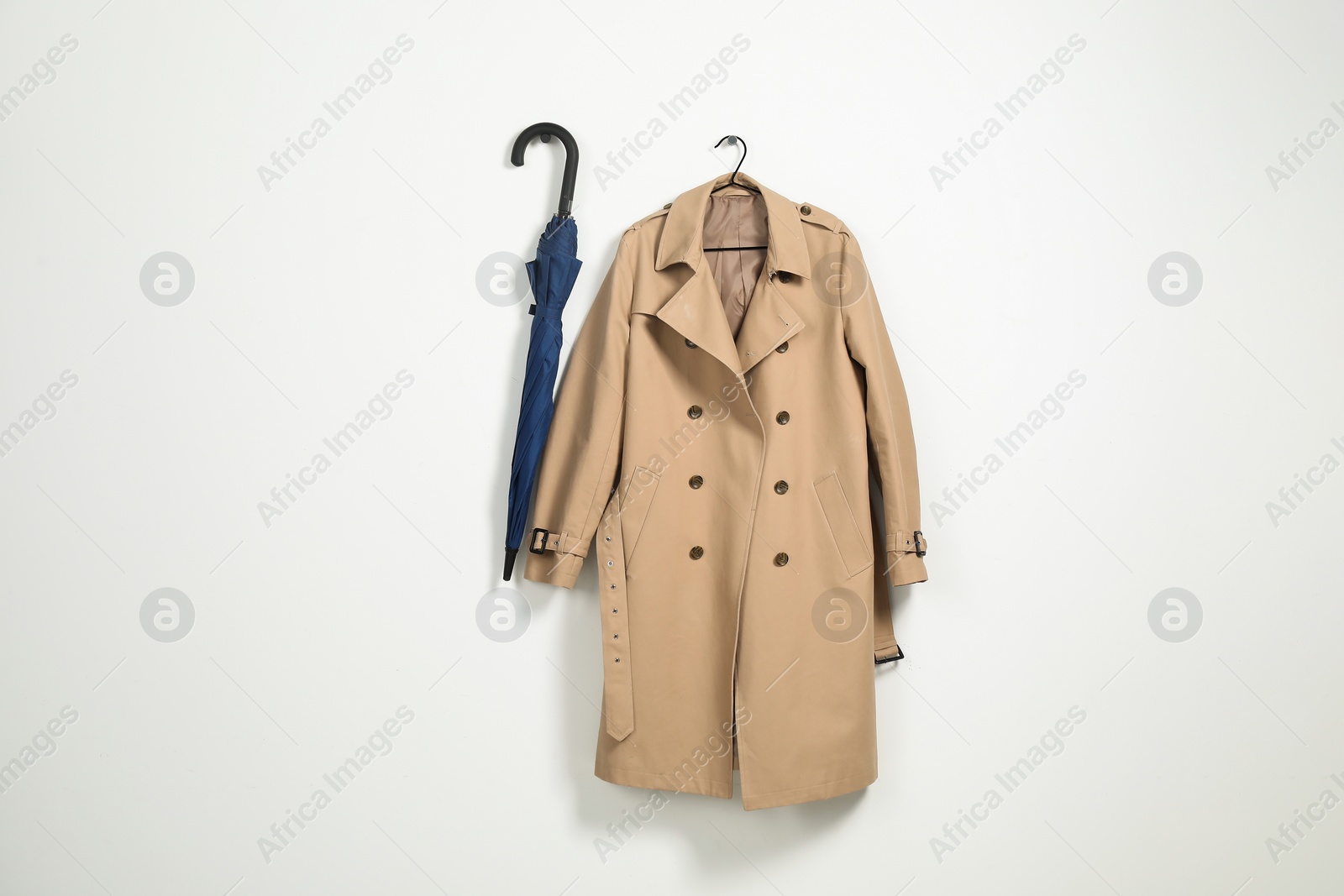 Photo of Hanger with beige trench coat and blue umbrella on white wall, space for text