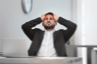 Image of Man suffering from migraine at workplace in office