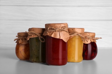 Photo of Jars with canned fruit jams on light grey table