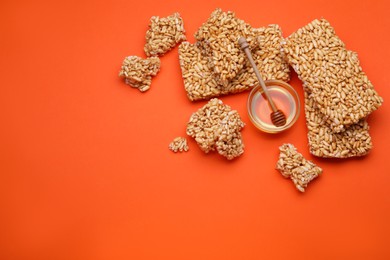 Photo of Puffed rice bars (kozinaki) and honey on orange background, flat lay. Space for text