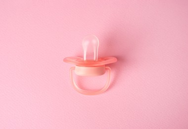 Photo of New baby pacifier on pink background, top view