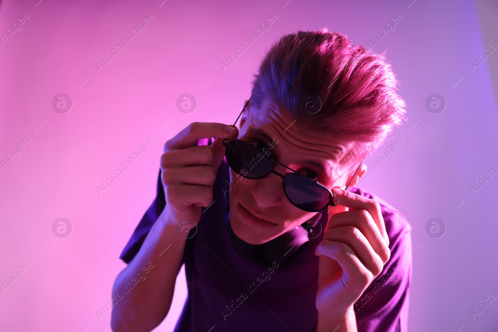 Photo of Young man with sunglasses on pink background in neon lights