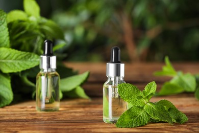 Photo of Bottles of mint essential oil and green leaves on wooden table