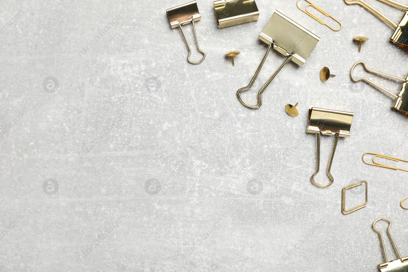 Photo of Golden binder clips and pins on light grey stone table, flat lay. Space for text