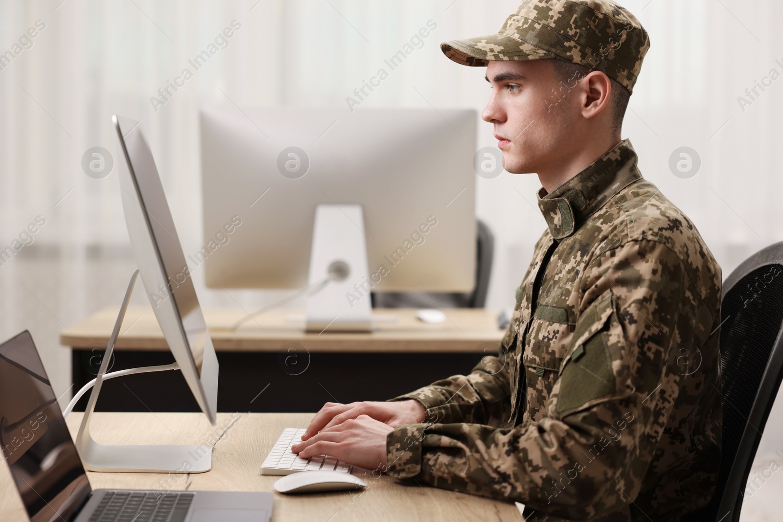 Photo of Military service. Young soldier working with computer at wooden table in office