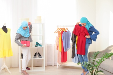 Photo of Muslim woman with her friend choosing clothes in modern shop