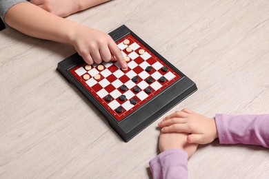 Photo of Children playing checkers at light wooden table, closeup