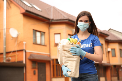 Photo of Female volunteer in protective mask and gloves with products on city street. Aid during coronavirus quarantine