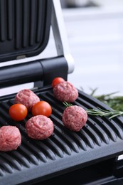 Photo of Meatballs, tomatoes and rosemary on electric grill, closeup