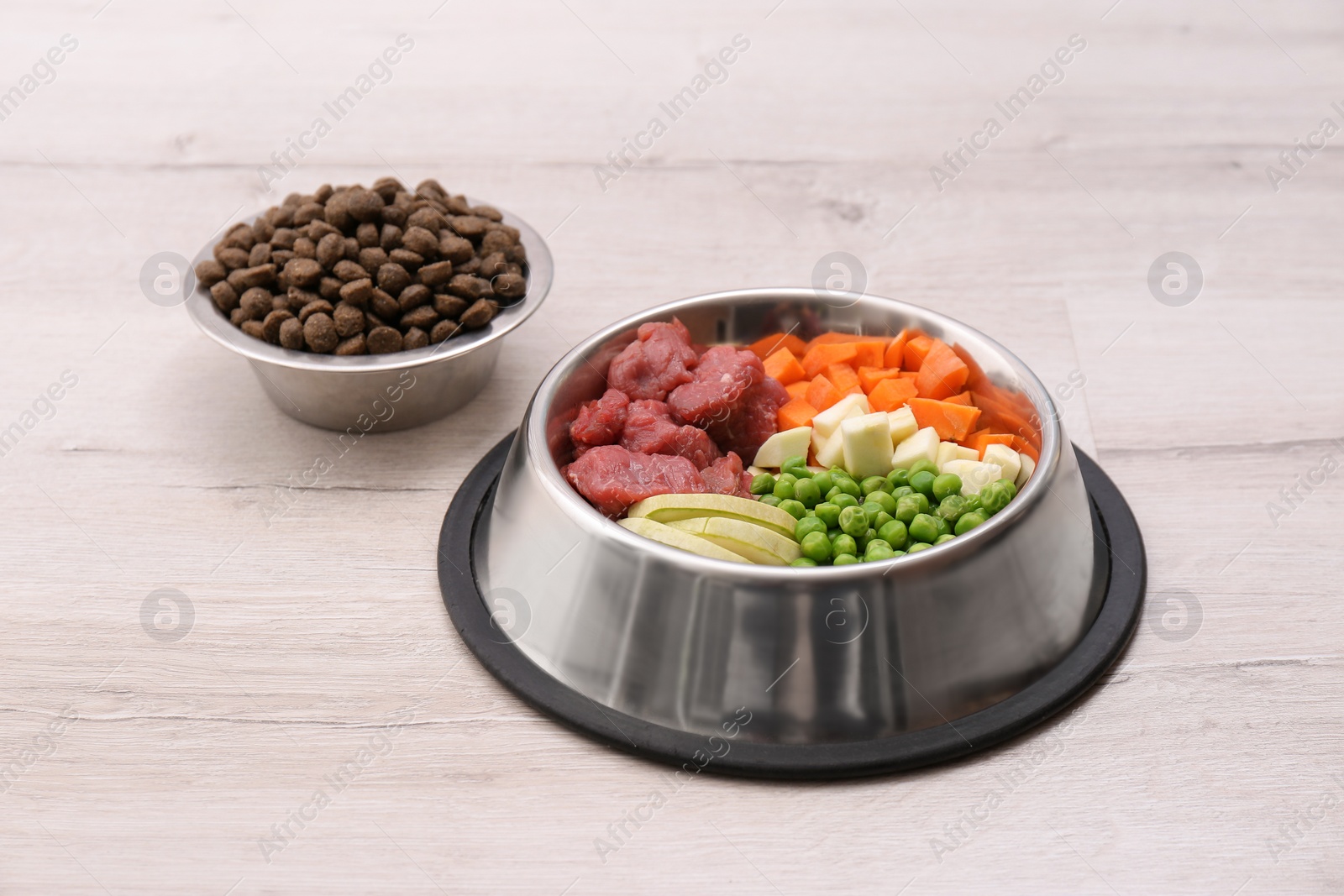 Photo of Bowls with dry and natural dog food on light background