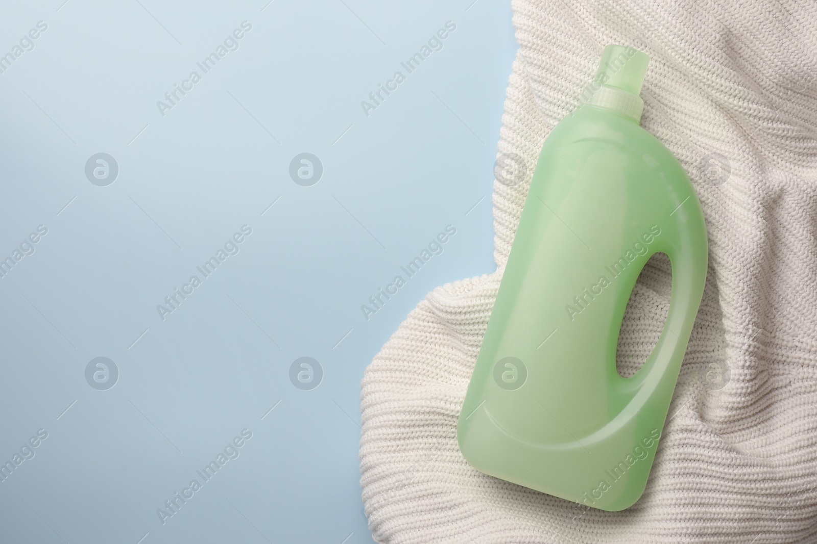 Bottle of fabric softener and white knitted cloth on light background, top view. Space for text Photo of Bottle of fabric softener and white knitted cloth on light background, top view. Space for text