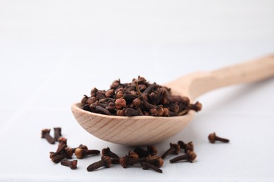 Spoon with aromatic dried clove buds on light table, closeup. Space for text