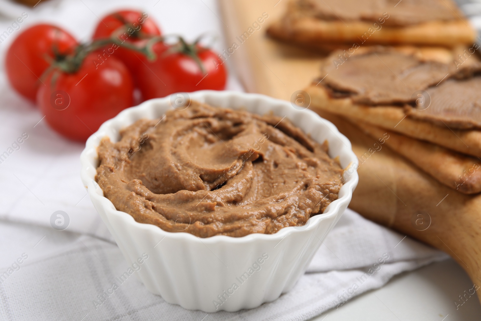 Photo of Delicious meat pate with tomatoes and crispy crackers on white table, closeup