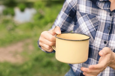 Photo of Young woman with drink in metal mug outdoors. Camping season