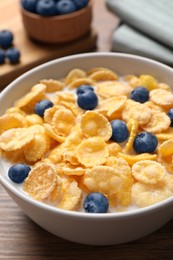 Photo of Bowl of tasty crispy corn flakes with milk and blueberries on wooden table, closeup