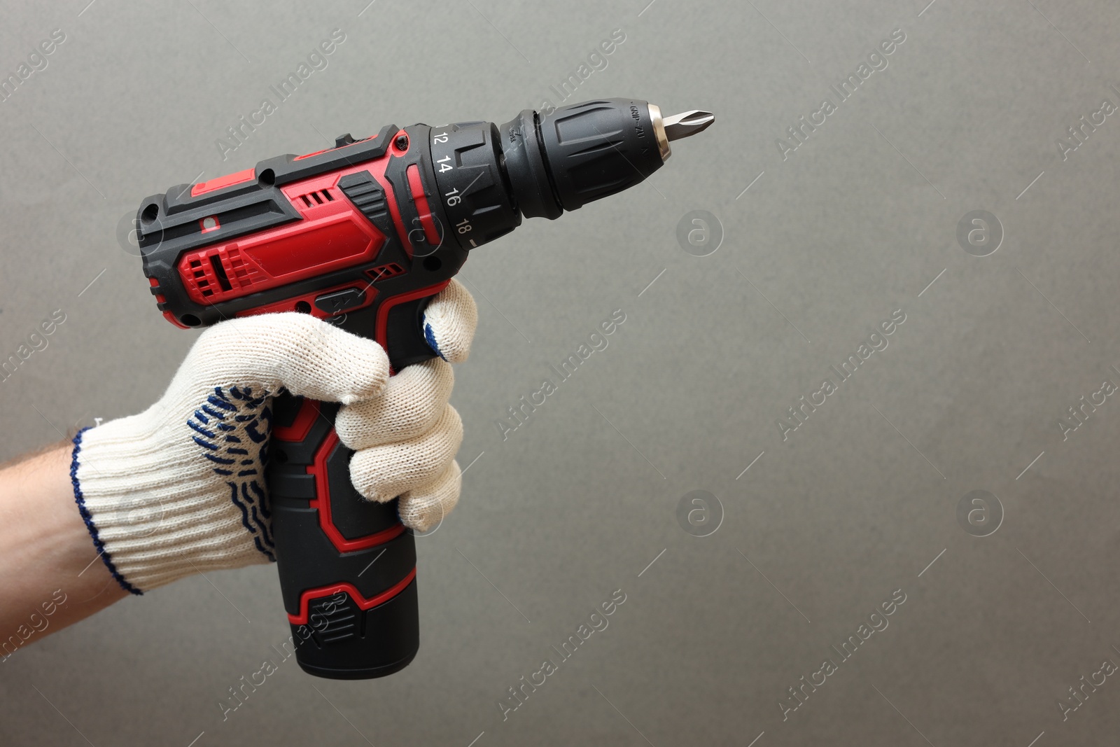 Photo of Handyman holding electric screwdriver on grey background, closeup. Space for text