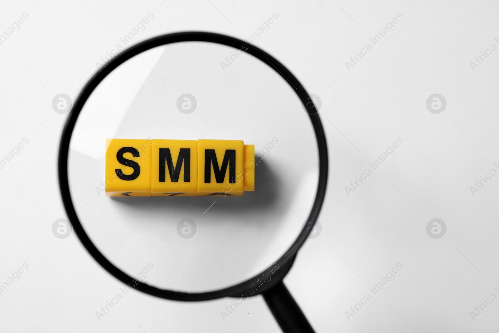 Photo of Top view through magnifying glass on yellow cubes with letters SMM, white background