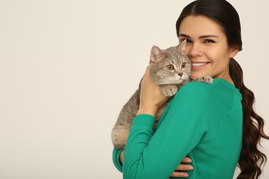 Young woman with adorable cat on light background