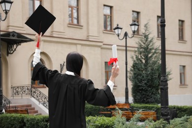 Photo of Student with diploma after graduation ceremony outdoors, back view. Space for text