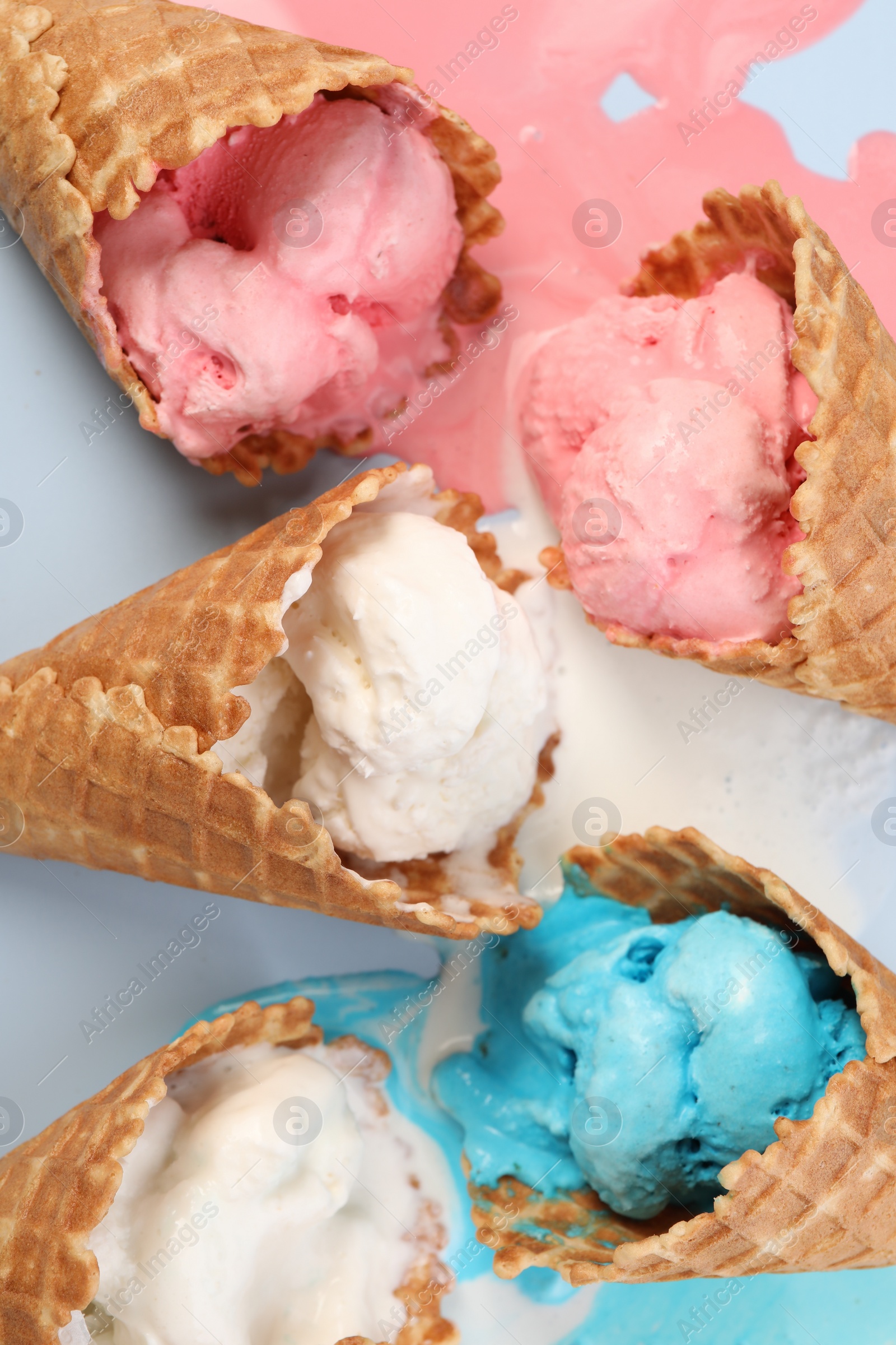 Photo of Melted ice cream in wafer cones on light blue background, flat lay