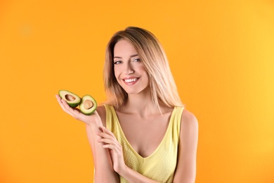 Portrait of young beautiful woman with ripe delicious avocado on color background