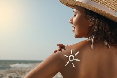 Photo of Beautiful African American woman with sun protection cream on shoulder at beach