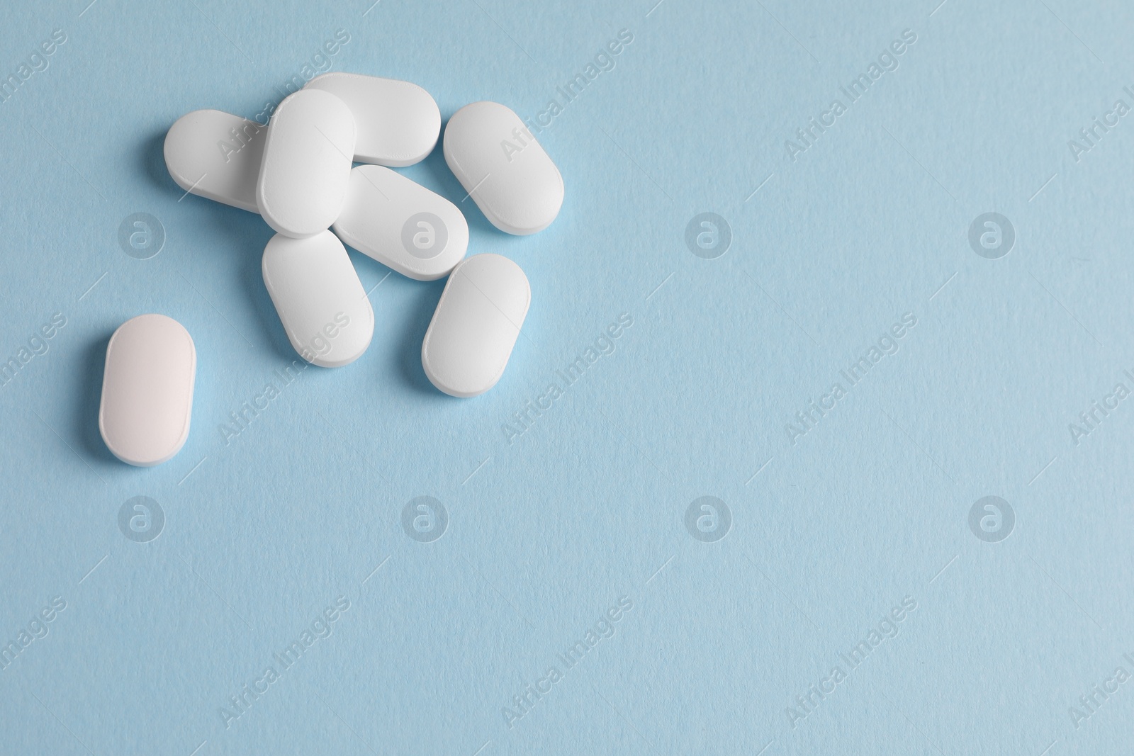 Photo of Pile of white pills on light blue background, flat lay. Space for text