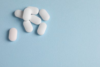 Pile of white pills on light blue background, flat lay. Space for text