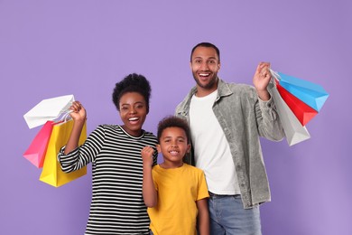 Photo of Family shopping. Happy parents and son with colorful bags on violet background
