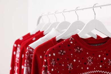 Rack with different Christmas sweaters on white background, closeup